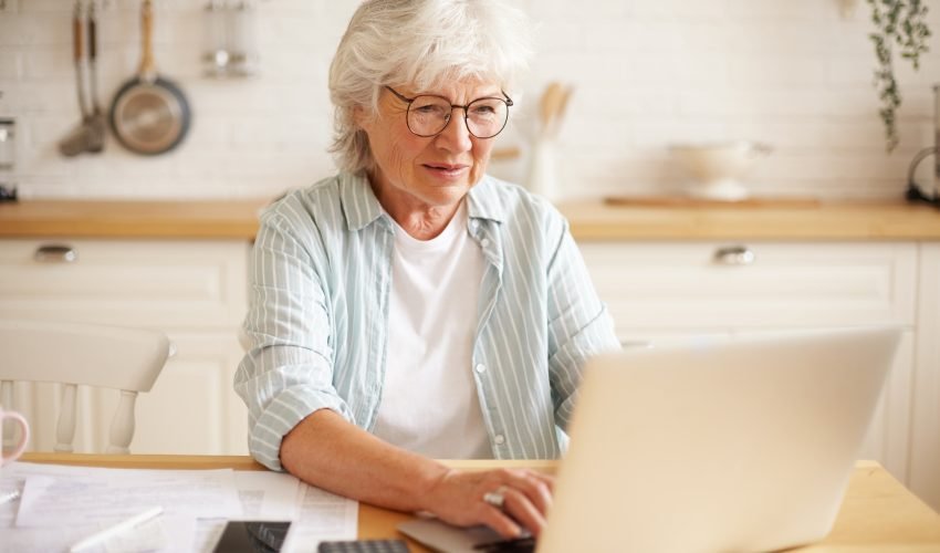 Aged people, electronic gadgets and lifestyle concept. Portrait of excited female on retirement shopping online using laptop. Elderly woman having happy look because she finally paid off all her debts