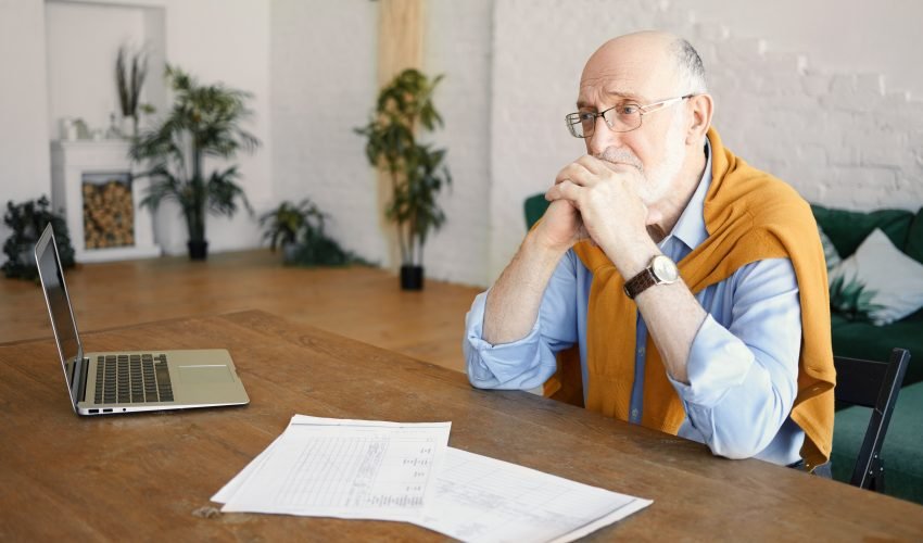 Indoor shot of unhappy sad senior bearded male entrepreneur sitt