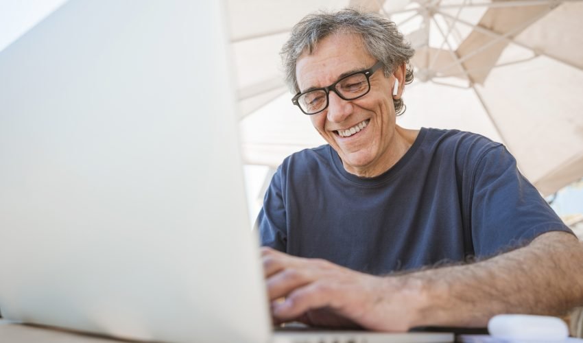 happy-senior-man-wearing-eyeglasses-using-laptop-outdoor-caf
