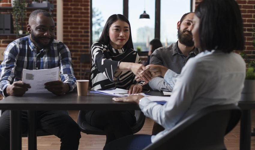 Marketing company recruiters sitting at desk in office while welcoming applicant to job interview.