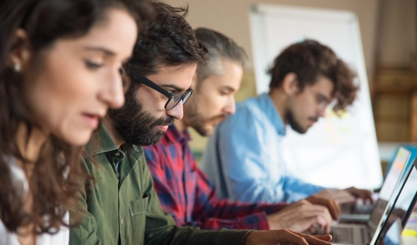 Line of coworkers using laptops in training room or class
