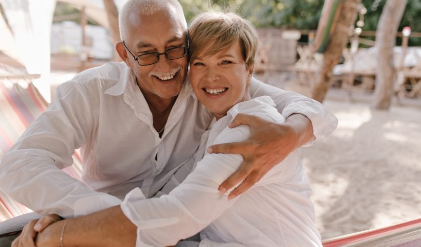 Positive man with gray mustache in eyeglasses and white shirt laughing and hugging his wife
