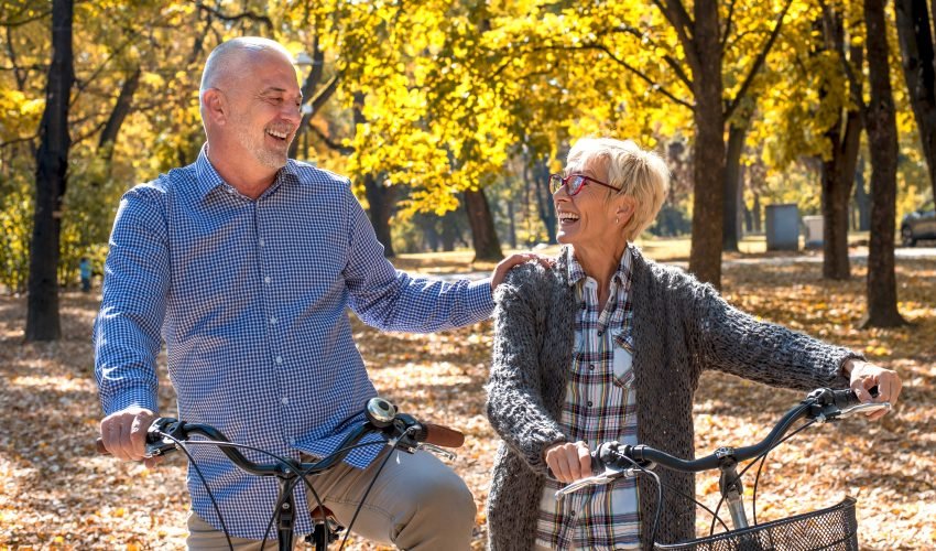 Happy elderly couple riding a bicycle in the park in the autumn