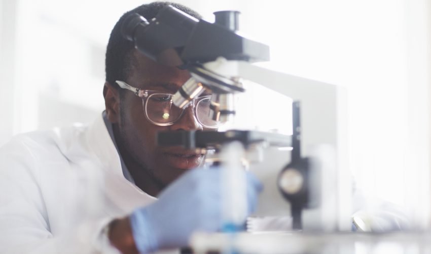 The scientist works with a microscope in a laboratory conducting experiments and formulas.