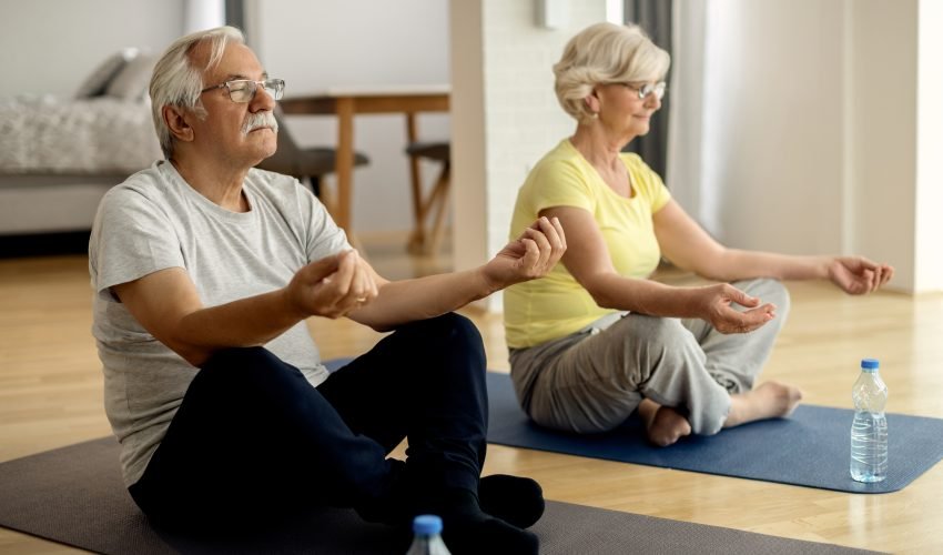 Mature couple meditating in lotus positing at home.