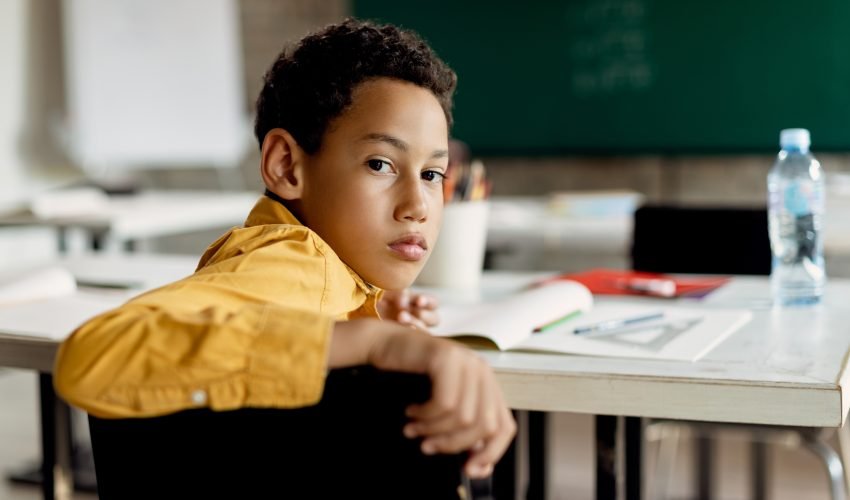 Black schoolboy turning to camera while sitting in the classroom
